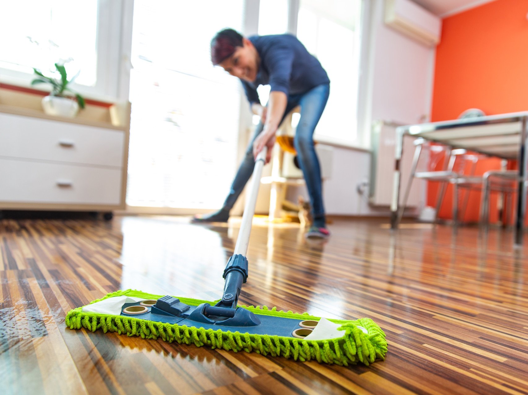 Nutzen Sie die Expertise unseres Fachbetriebs in Gronau für das fachgerechte Verlegen Ihres Laminatbodens, um ein perfektes und langlebiges Finish zu erzielen. Wir garantieren Ihnen eine präzise Ausführung und beraten Sie umfassend zur optimalen Vorbereitung Ihres Untergrunds für maximalen Wohnkomfort.  Bildbeschreibung: Eine Nahaufnahme zeigt die Hände einer Person, die eine Laminatdiele in heller Eichenoptik verlegt. Das Paneel wird in einem schrägen Winkel angesetzt, um es in die Nut-Feder-Verbindung der bereits am Boden liegenden Dielen einzuklicken. Unter dem Laminat ist eine weiße Schaumstoff-Trittschalldämmung erkennbar, während der Hintergrund der Baustellensituation in Unschärfe verschwimmt.